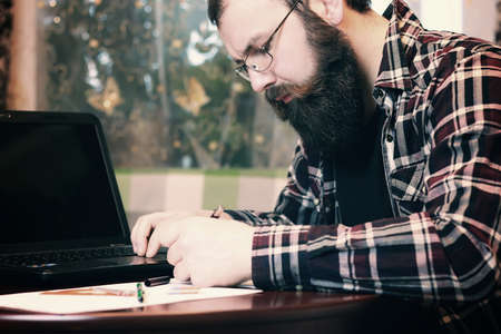 bearded man sitting at a table and working with a laptopの写真素材