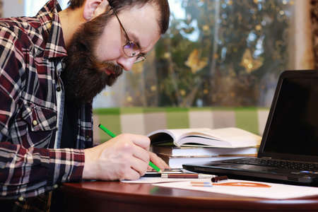 bearded man sitting at a table and working with a laptopの写真素材
