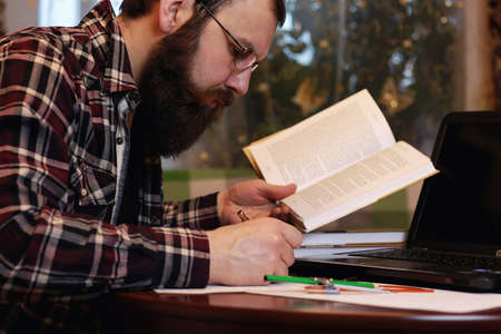 bearded man sitting at a table and working with a laptopの写真素材