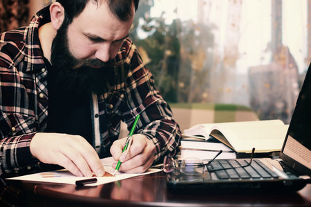 bearded man sitting at a table and working with a laptopの写真素材