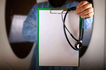 Doctor in blue robe holding a tablet for notes and a stethoscope in the hands ofの写真素材