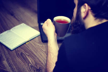 bearded handsome man lies on the floor wrapped in a plaid, and working at a laptopの写真素材