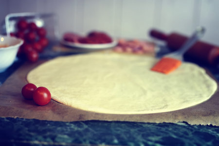 dough for pizza with cherry tomatoes and basil smoked sausageの写真素材