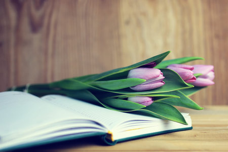 still life on the texture old wooden table bouquet of beautiful tulips an open bookの写真素材