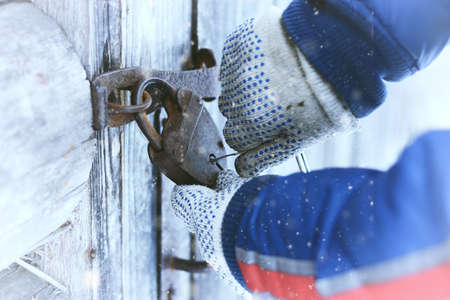 man's hands closed old rusty padlock on an old wooden door of the houseの写真素材