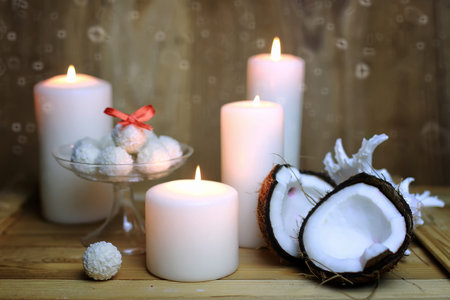 little sweet candies in coconut flakes and surrounded by burning candles and fresh coconutの写真素材