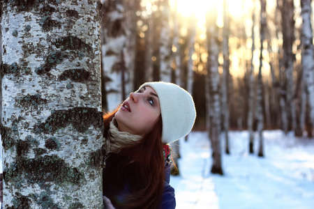 Pretty red-haired girl in the winter forest walks in the snow on a sunny dayの写真素材