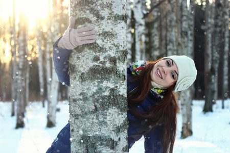 Pretty red-haired girl in the winter forest walks in the snow on a sunny dayの写真素材