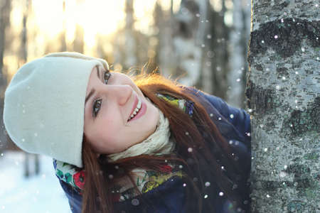 Pretty red-haired girl in the winter forest walks in the snow on a sunny dayの写真素材