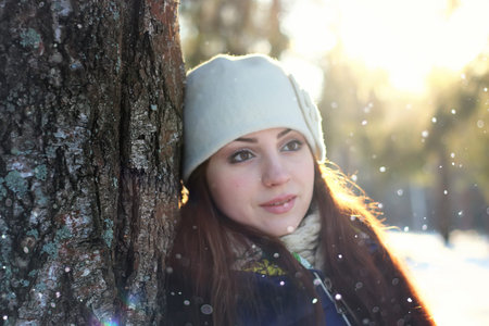 Pretty red-haired girl in the winter forest walks in the snow on a sunny dayの写真素材