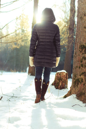 Pretty red-haired girl in the winter forest walks in the snow on a sunny day