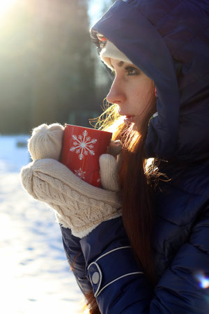 Pretty red-haired girl in the winter forest walks in the snow on a sunny day