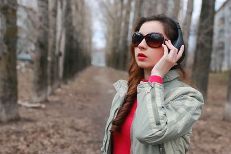 good-looking student listening to music on headphones walking through autumn park of tall treesの写真素材