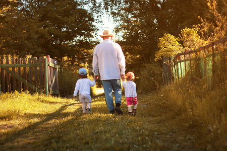 young grandfather bringing up grandchildren on his country area on a summer eveningの写真素材