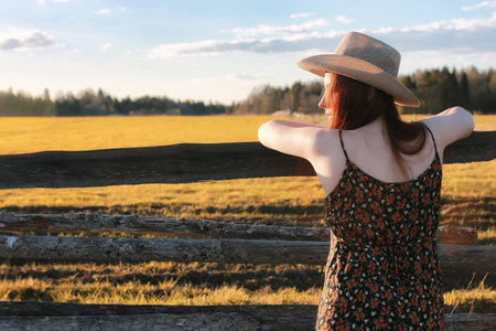 young sweet girl in a cowboy hat and red coat on a warm day in spring natureの写真素材