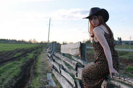 young sweet girl in a cowboy hat and red coat on a warm day in spring natureの写真素材