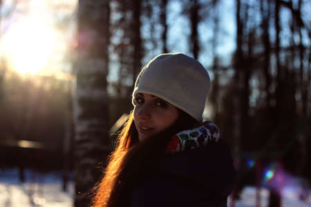 Pretty red-haired girl in the winter forest walks in the snow on a sunny dayの写真素材