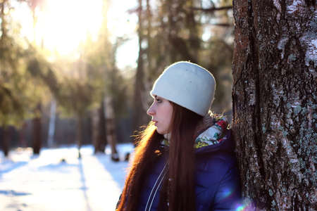 Pretty red-haired girl in the winter forest walks in the snow on a sunny dayの写真素材