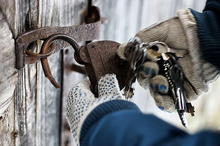 man's hands closed old rusty padlock on an old wooden door of the houseの写真素材