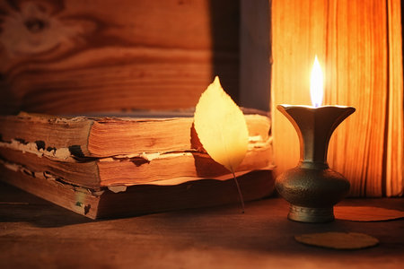 stack of old tattered book on a wooden table lighted candle and glasses