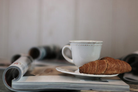 breakfast French-style hot coffee and fresh croissant and a soft pile of glossy magazines on the tableの写真素材