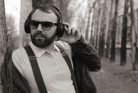 good-looking student listening to music on headphones walking through autumn park of tall treesの写真素材