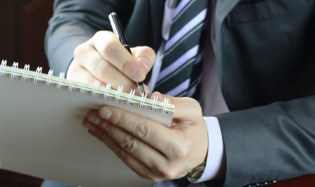 a man in the strict business suit sitting with a notebook and making notesの写真素材