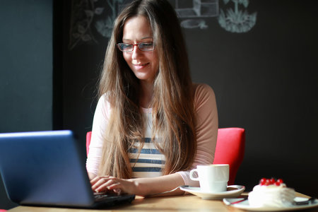 portrait of cute girl working on a laptop and drinking coffee in a cafeの写真素材