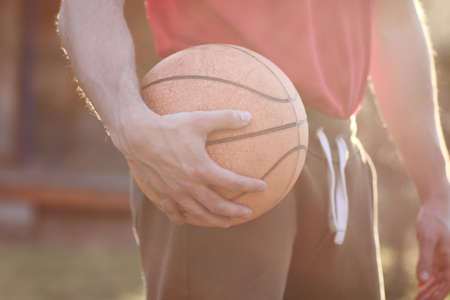 man hand hold basketball ball in sunny evening in summerの写真素材