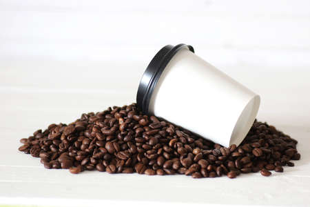 coffe in a white paper cup and beans on a tableの写真素材