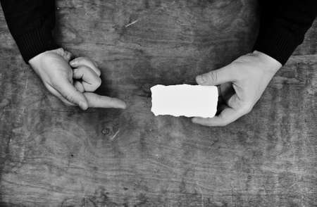 male hands holding a white blank sheet of paper on the background of wooden texture tableの写真素材