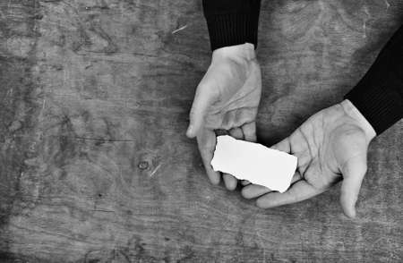 male hands holding a white blank sheet of paper on the background of wooden texture tableの写真素材
