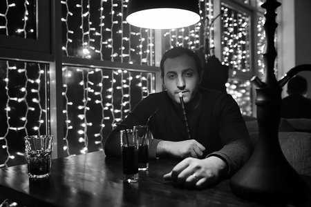 man holding hookah pipe and smoking in a night club