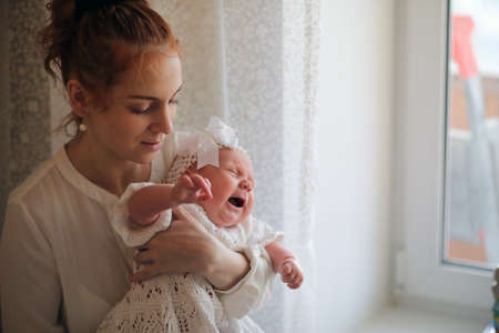 young mother and newborn baby in her arms standing by the windowの写真素材