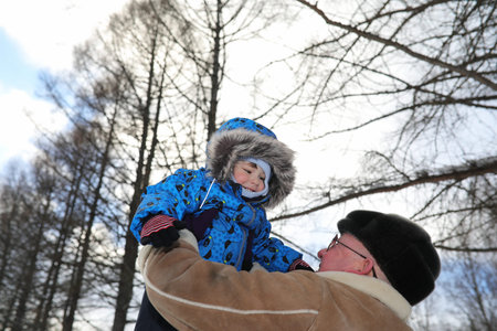 Parent holding kid on hands in winter parkの写真素材