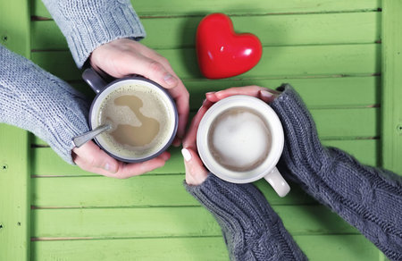 Young couple drinking hot coffee at a wooden table on a dateの写真素材
