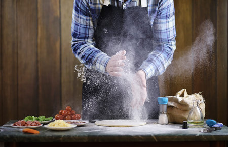 a man preparing a pizza, knead the dough and puts ingredientsの写真素材