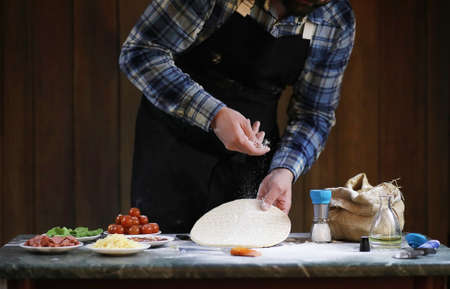 a man preparing a pizza, knead the dough and puts ingredientsの写真素材