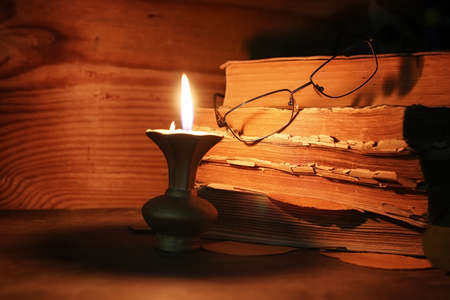 old tattered book on a wooden table lighted candle and glassesの写真素材