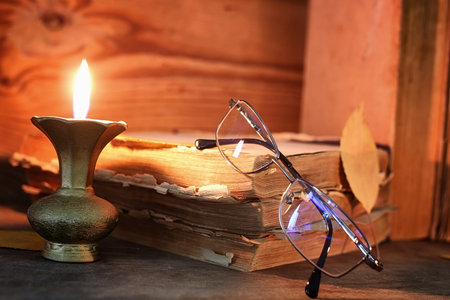 old tattered book on a wooden table lighted candle and glassesの写真素材