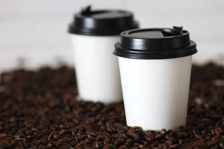 coffe in a white paper cup and beans on a tableの写真素材