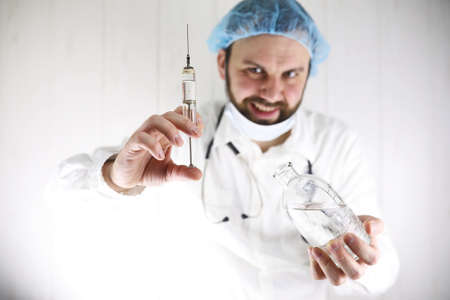 Crazy bearded doctor in a white coat and old syringeの写真素材