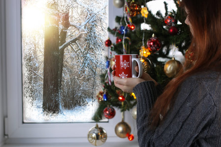 Girl with a cup of hot drink stands in front of a windowの写真素材