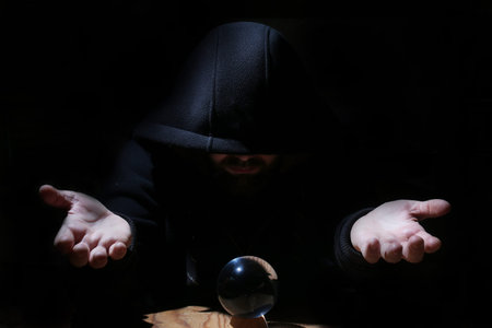 man in a black hood with cristal ball