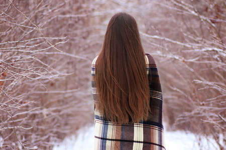 cute girl with blue eyes wrapped in a blanket in the winter outside in the parkの写真素材