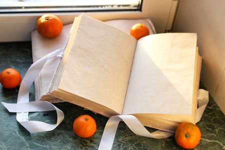 tangerines and vintage books on a marble table by the windowの写真素材