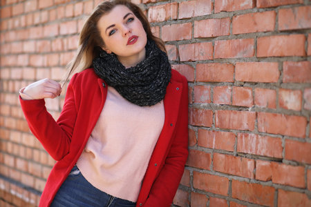 Cute girl in red coat on brick wallの写真素材
