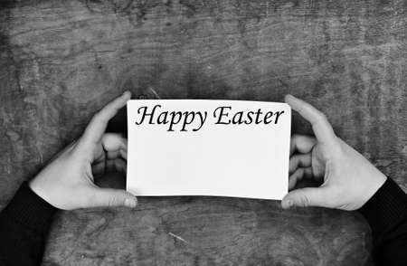 male hands holding a white sheet of paper on the background of wooden texture table happy easter themeの写真素材