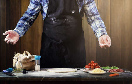 a man preparing a pizza, knead the dough and puts ingredientsの写真素材