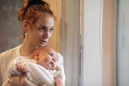 young mother and newborn baby in her arms standing by the windowの写真素材